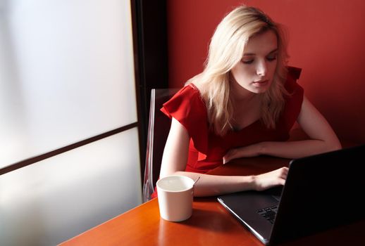 Young adult woman wearing red jumpsuit and using laptop