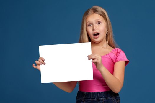 Portrait of adorable blonde little girl on blue background. in pink shirt, holding horizontal white copy space