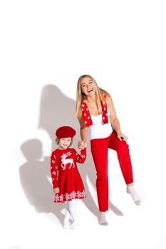 Stock photo of cheerful blonde mother in red pants, white top and red scarf holding daughter s hand. Daughter wearing red winter dress and beret. Studio shot.