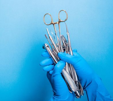 Hand in blue glove holding surgery dental tools on light blue background