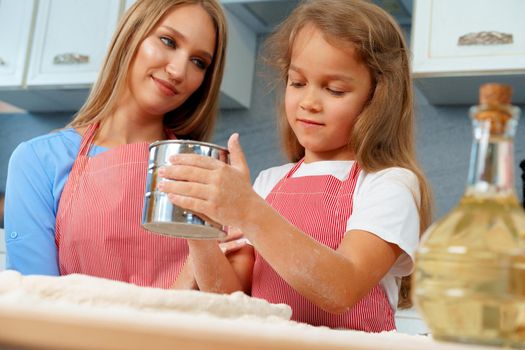 Mother and her little daughter preparing dough in kitchen close up