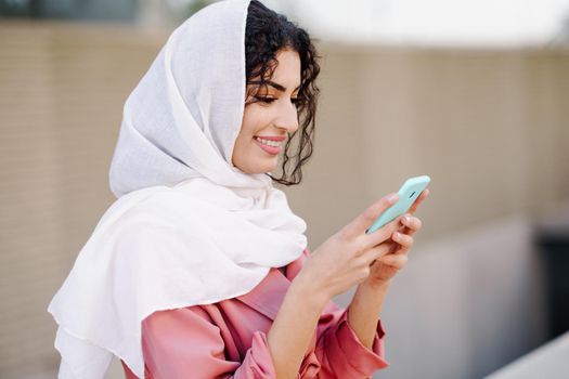 Young Arab woman wearing hijab headscarf texting message with her smartphone in urban background.