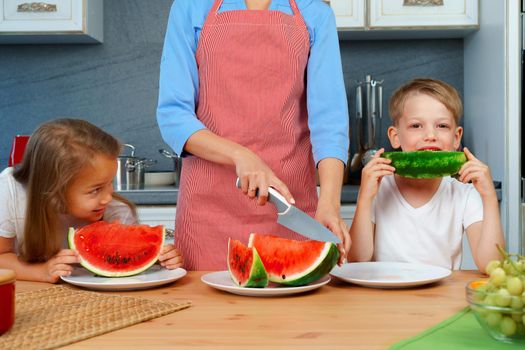 Sweet family, mother and her kids eating watermelon in their kitchen having fun, close up