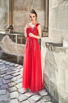 Beautiful bridesmaid brunette girl ladywearing elegant full length red chiffon bridesmaid dress with lace and holding flower bouquets. European old town location for wedding day.