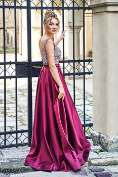 Two beautiful bridesmaids girls blonde and brunette ladies wearing elegant full length purple violet lilac lavender satin bridesmaid dress with silver sequined camisole top. European old town location for wedding day.