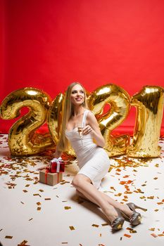 cheerful caucasian young female holds a small red box with a christmas present in her hands, picture isolated on red background