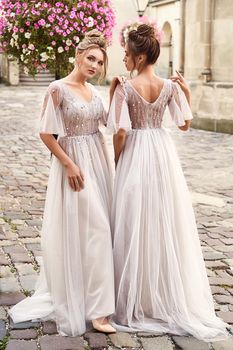 Beautiful bridesmaids in gorgeous light silver dresses in old beautiful European city on a wedding day in summer. Dresses are floor length or full-lenghth long tulle with half sheer sleeves and side slit.