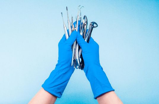 Hand in blue glove holding surgery dental tools on light blue background