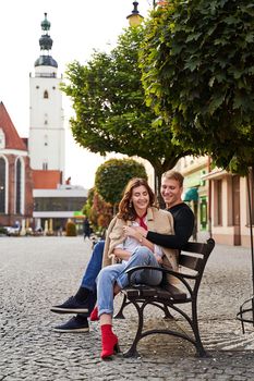 Beautiful young caucasian couple cuddling on a bench in a European town. Romatnic date and love concept.