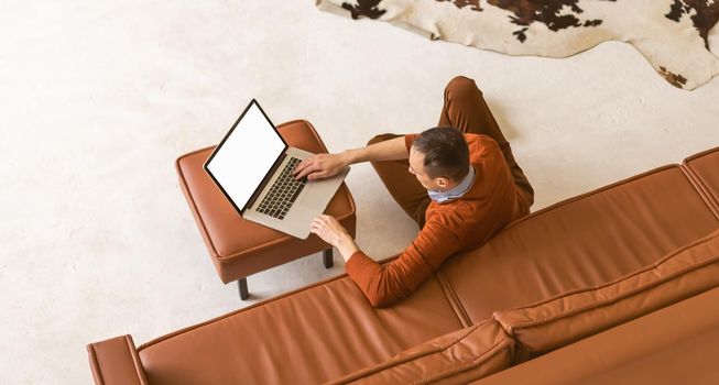 Man using notebook with blank screen in living room.