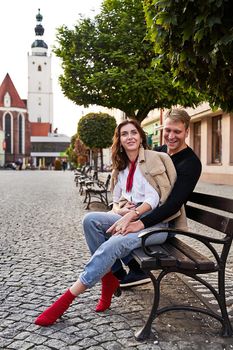 Beautiful young caucasian couple cuddling on a bench in a European town. Romatnic date and love concept.