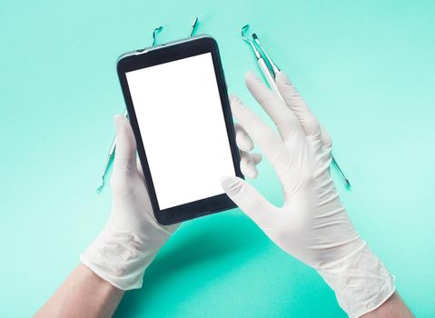 Top view of hands in gloves holding smartphone on light turquoise background with dental tools