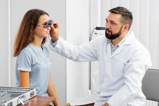 Doctor holding special eye equipment examinating girl's eyes in the ophthalmologic clinic