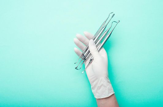 Hand in glove holding dental tools on light turquoise background