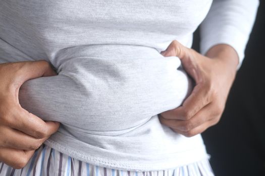 man's hand holding excessive belly fat, overweight concept.