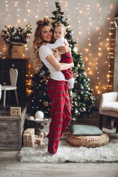 Full length portrait of attractive young mother holding baby daughter against Christmas tree.