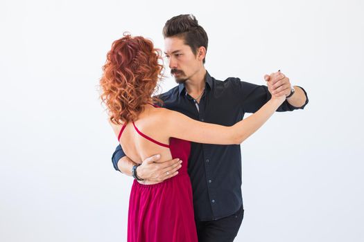 Social dance, bachata, kizomba, salsa, tango concept - Woman dressed in red dress and man in a black costume over white background.