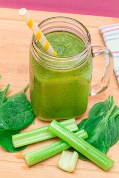 Fresh Green Smoothie of Apple, Celery, and Spinach in Glass Smoothie Jar with Yellow Cocktail Straw on Wooden Cutting Board. Vegan Detox Drink. Vegetarian Culture. Healthy Eating and Fruit Diet