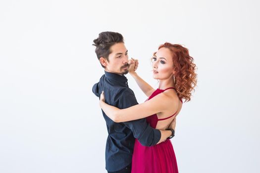 Social dance, bachata, kizomba, salsa, tango concept - Woman dressed in red dress and man in a black costume over white background.