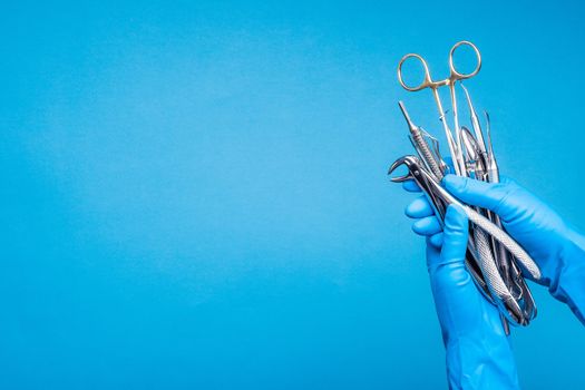 Hand in blue glove holding surgery dental tools on light blue background