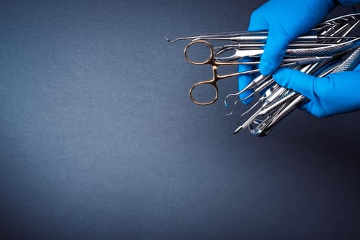 Hands in blue gloves holding metal dental equipment on gray background with copy space