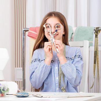 Cute young tailor with scissors at workspace