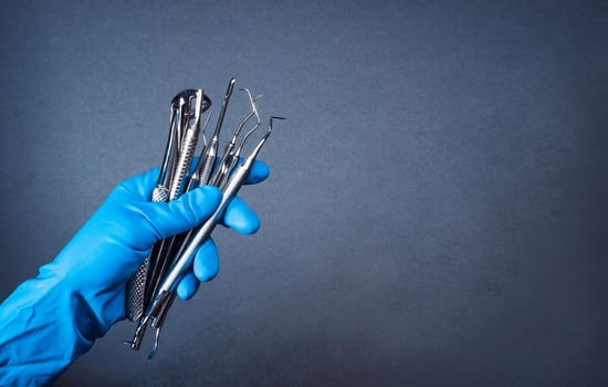 Hands in blue gloves holding metal dental equipment on gray background with copy space