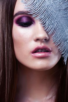beauty brunette young girl with fashion makeup and silver feather close up on white background