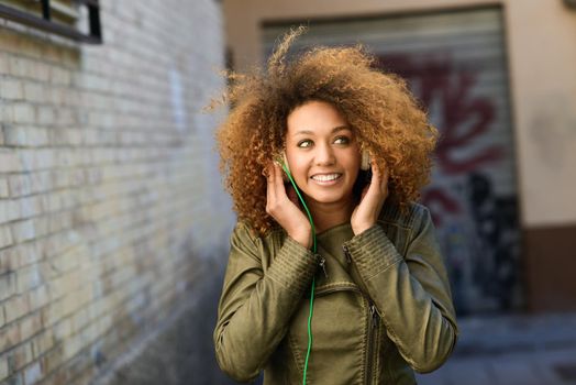 Portrait of young attractive black girl in urban background hearing music with headphones
