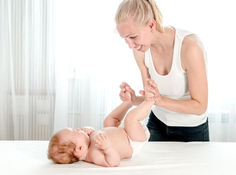 Mother massaging her infant baby. Happy mother playing with newborn baby in bedroom. Mothers love, maternity concept