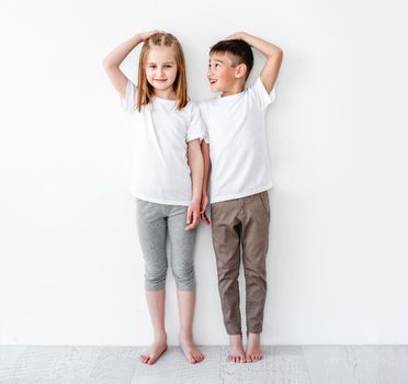 children measuring height and comparing on white wall background