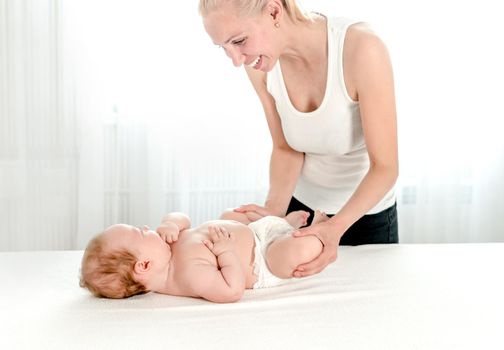 Mother massaging her infant baby. Happy mother playing with newborn baby in bedroom. Mothers love, maternity concept