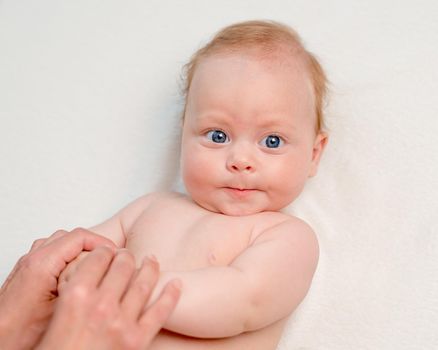 Mother doing body massage or gymnastics for baby's hands with cute infant baby lying on the white bed. Mother's care concept