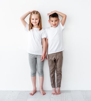 children measuring height and comparing on white wall background