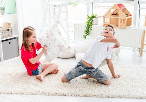 Pretty little boy ang girl fighting pillows in modern playroom