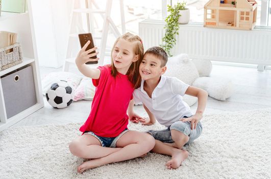 Happy boy and girl children taking selfie on smartphone in kids room