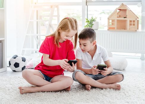Smiling children looking at smartphone sitting in playroom