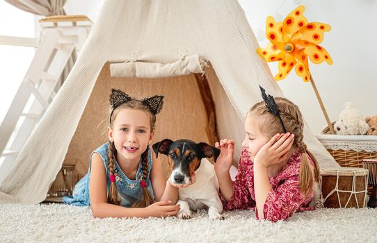 Children girls lying with fox terrier dog in wigwam at home