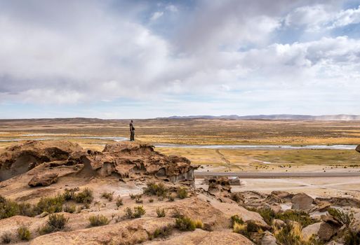 Man standing on the edge of rocky hill and taking pleasure of spacious Bolivian landscape