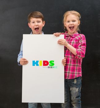 two cute smiling schoolchildren with blank sheet of paper in hands on a black background