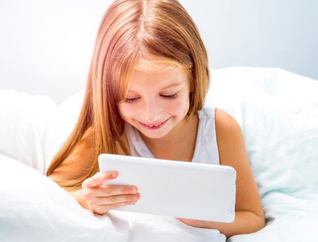 little schoolgirl with tablet lies in bed at home