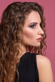 Portrait of beautiful young blonde girl in black dress on pink background. Fashion photo. The model looks aside