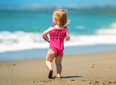cute baby girl playing on the beach at sunset