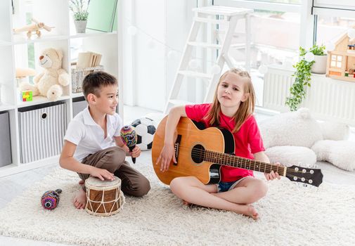 Smiling kids playing on drum and guitar in modern apartment