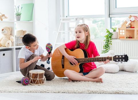 Smiling kids playing on drum and guitar in modern apartment