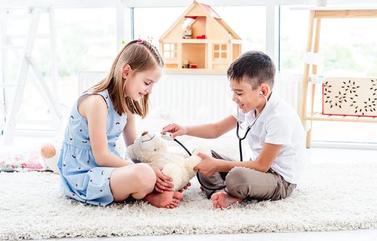 Smiling children playing doctor with teddy bear in bright room