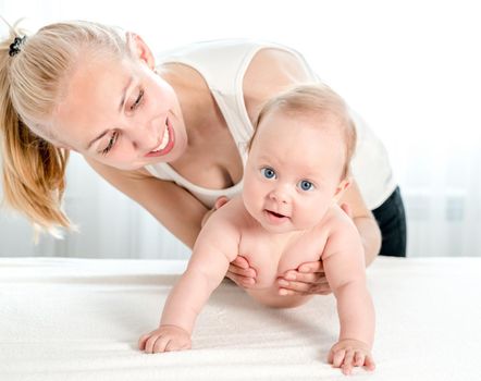 Smiling young mother holding her little newborn baby. Young mother playing with her lovely child at home