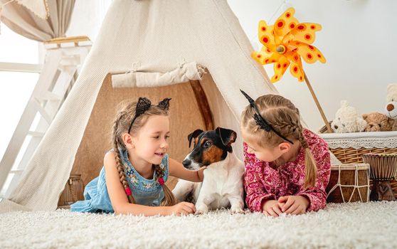 Children girls lying with fox terrier dog in wigwam at home
