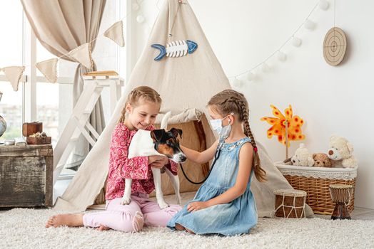 Little girls with phonendoscope listening dog like doctor sitting on floor in playroom