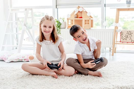 Cute little girl and boy with joysticks playing on console indoors